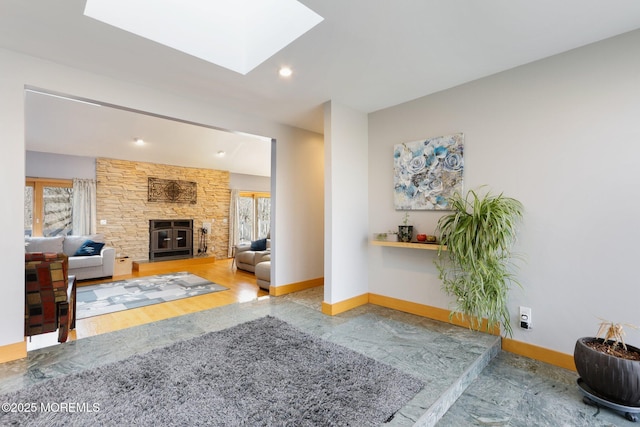 living room with a stone fireplace, recessed lighting, a skylight, wood finished floors, and baseboards