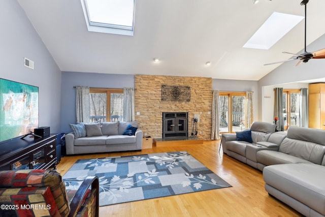 living room with a skylight, visible vents, a stone fireplace, wood finished floors, and high vaulted ceiling