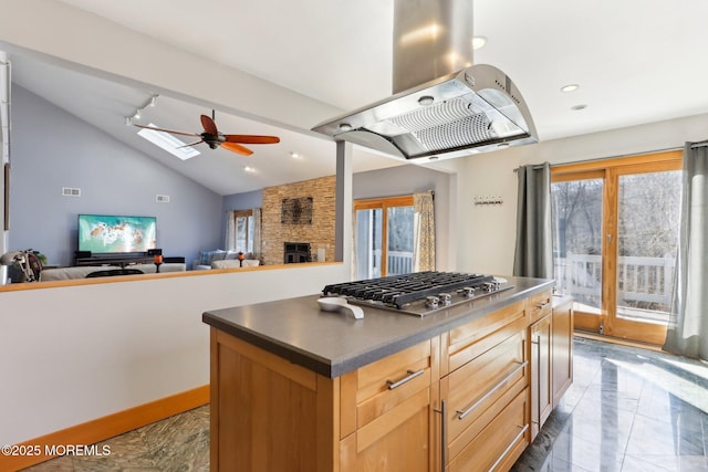 kitchen featuring island range hood, lofted ceiling with skylight, open floor plan, a stone fireplace, and stainless steel gas cooktop