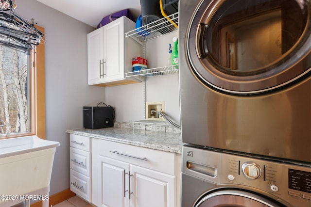 clothes washing area featuring a healthy amount of sunlight, cabinet space, and stacked washing maching and dryer