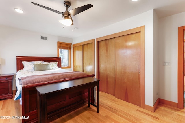 bedroom with visible vents, light wood-style flooring, baseboards, and two closets