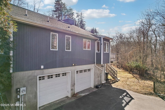 view of side of property with a garage, a chimney, stairway, aphalt driveway, and roof with shingles