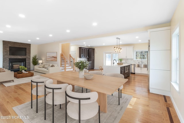 dining area featuring sink, a chandelier, a fireplace, and light wood-type flooring