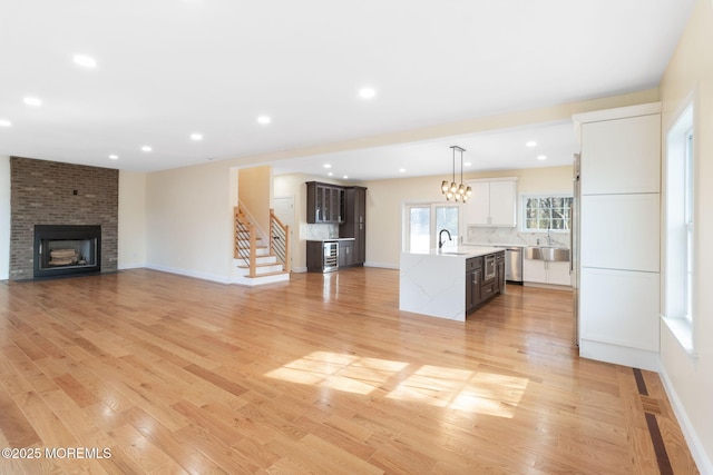 kitchen with hanging light fixtures, an island with sink, dark brown cabinetry, and light hardwood / wood-style flooring