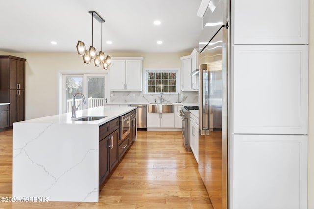 kitchen with decorative light fixtures, high quality appliances, white cabinetry, sink, and a kitchen island with sink