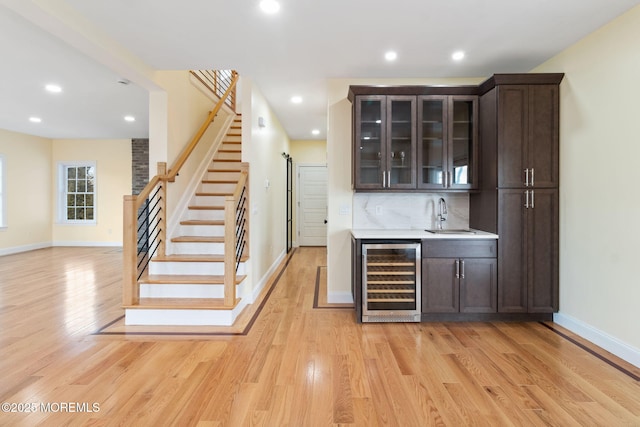 bar with dark brown cabinets, sink, beverage cooler, and light wood-type flooring