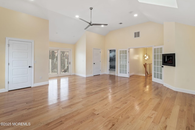 unfurnished living room with ceiling fan, a skylight, high vaulted ceiling, light hardwood / wood-style floors, and french doors