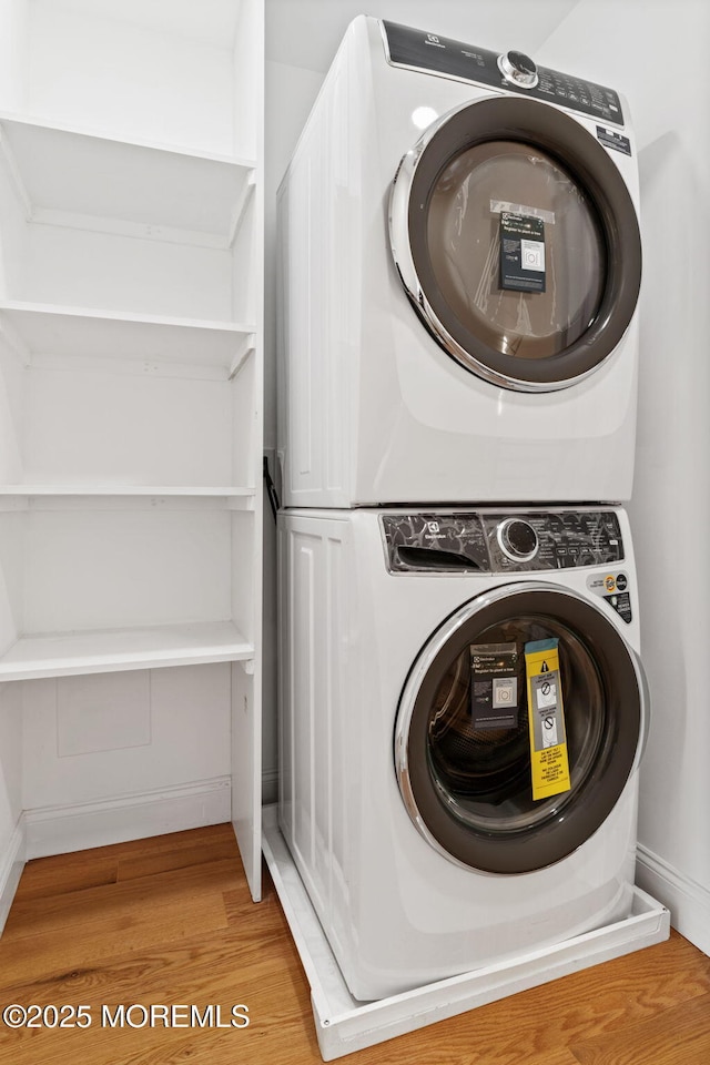 clothes washing area featuring stacked washer / drying machine and wood-type flooring