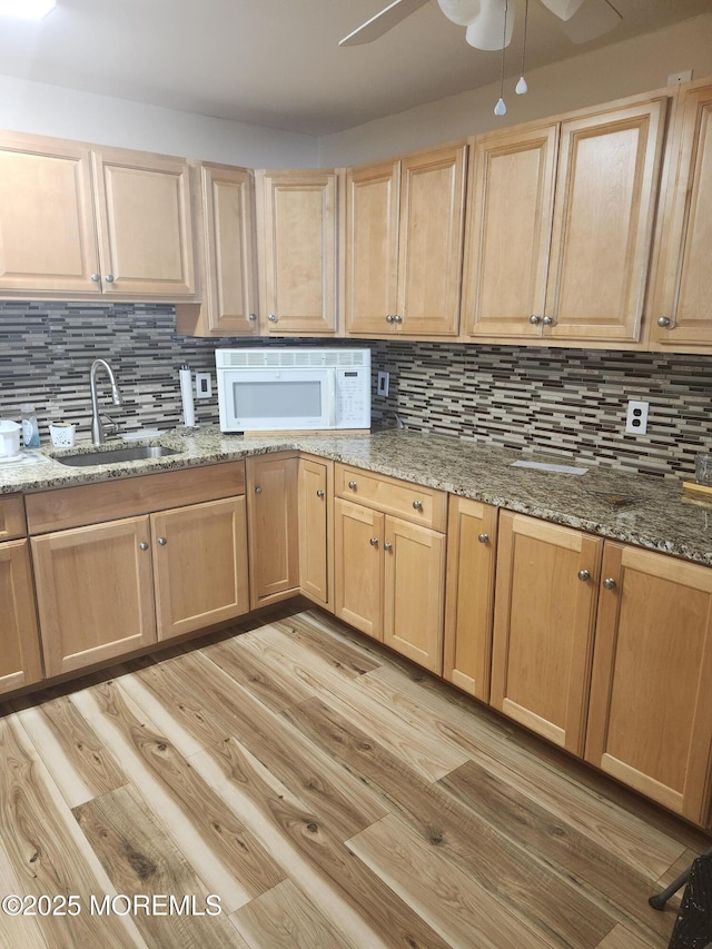 kitchen with light hardwood / wood-style flooring, sink, stone counters, ceiling fan, and tasteful backsplash