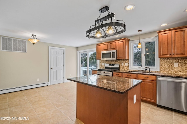 kitchen featuring sink, hanging light fixtures, stainless steel appliances, a center island, and dark stone counters