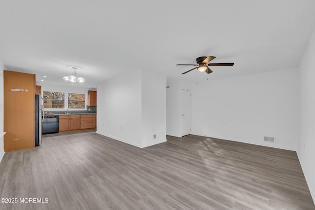 unfurnished living room featuring wood-type flooring, sink, and ceiling fan with notable chandelier