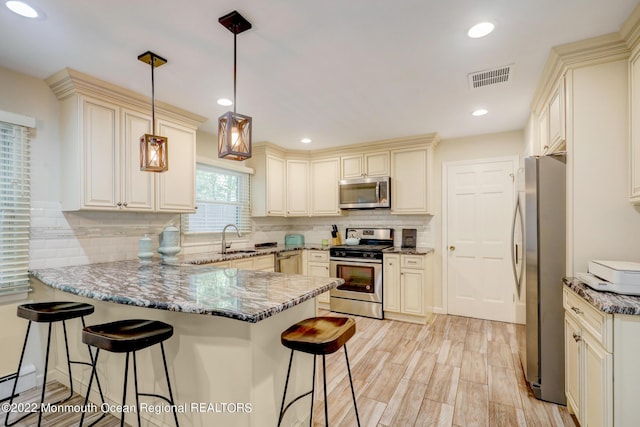 kitchen with visible vents, stone counters, a peninsula, cream cabinetry, and stainless steel appliances