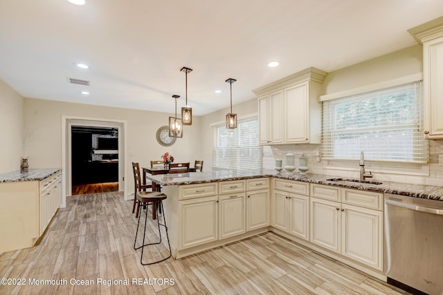 kitchen with visible vents, a peninsula, a sink, stainless steel dishwasher, and cream cabinets