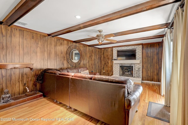 living area with a ceiling fan, wood finished floors, beam ceiling, wood walls, and a brick fireplace