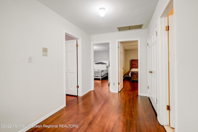 hallway featuring visible vents, attic access, dark wood-type flooring, and baseboards