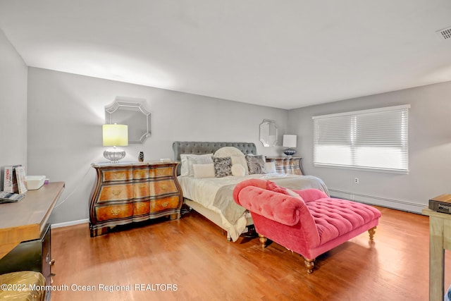 bedroom featuring a baseboard heating unit, visible vents, wood finished floors, and baseboards