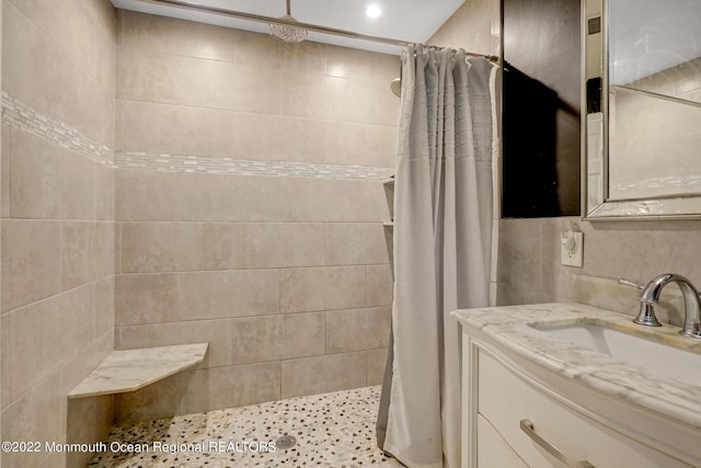 full bathroom with tile walls, vanity, and a tile shower