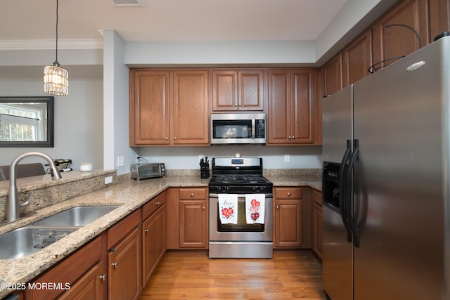 kitchen with sink, appliances with stainless steel finishes, hanging light fixtures, light stone counters, and light hardwood / wood-style floors