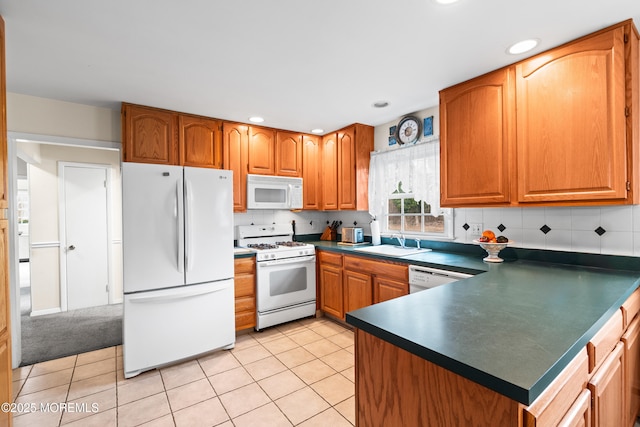 kitchen featuring white appliances, light tile patterned floors, dark countertops, brown cabinets, and a sink