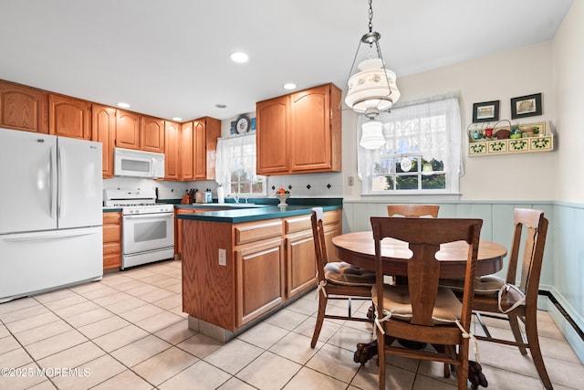 kitchen featuring white appliances, a wainscoted wall, a peninsula, and light tile patterned floors