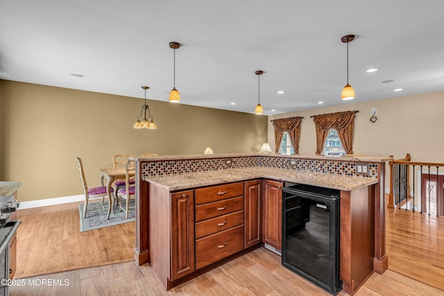 kitchen featuring wine cooler, light stone counters, hanging light fixtures, and light wood-type flooring