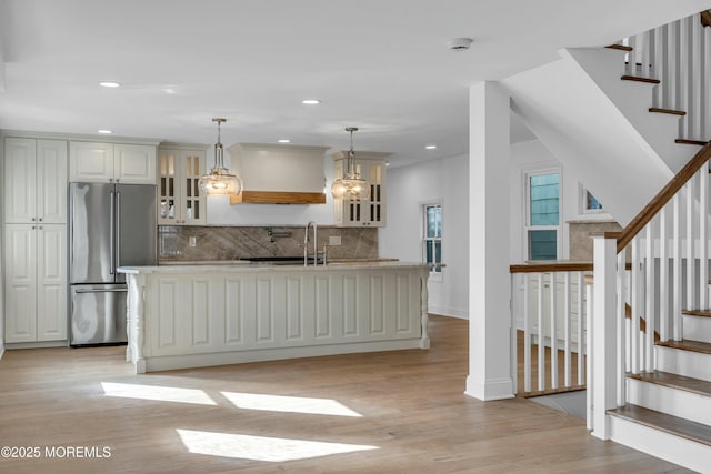 kitchen with light hardwood / wood-style flooring, hanging light fixtures, tasteful backsplash, a center island with sink, and high end refrigerator