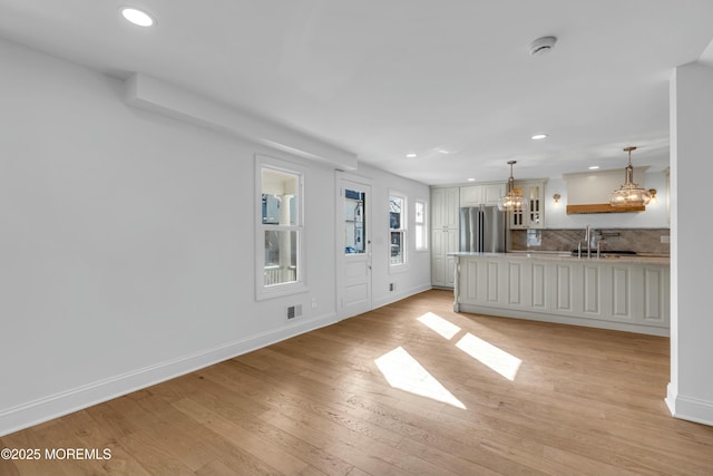 unfurnished living room featuring sink, a chandelier, and light wood-type flooring