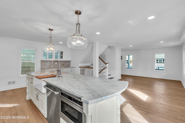 kitchen featuring white cabinetry, pendant lighting, light wood-type flooring, and a center island with sink