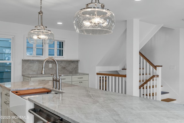 kitchen with sink, an inviting chandelier, light stone countertops, white cabinets, and decorative backsplash