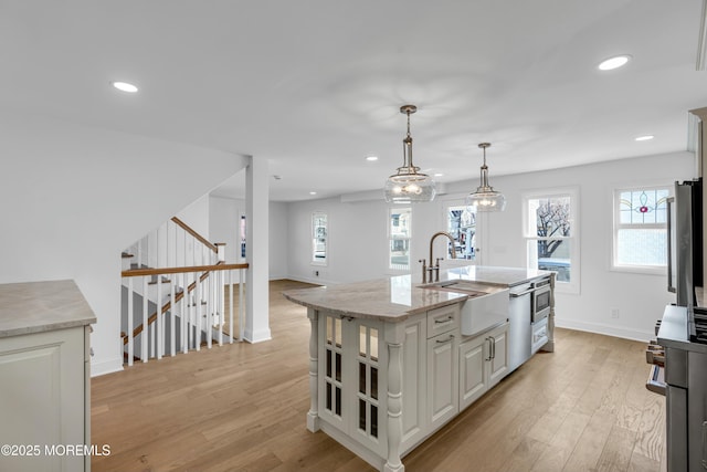 kitchen featuring decorative light fixtures, white cabinetry, sink, a kitchen island with sink, and light stone counters