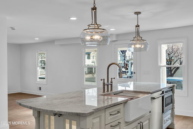 kitchen featuring white cabinetry, hanging light fixtures, light hardwood / wood-style flooring, and an island with sink