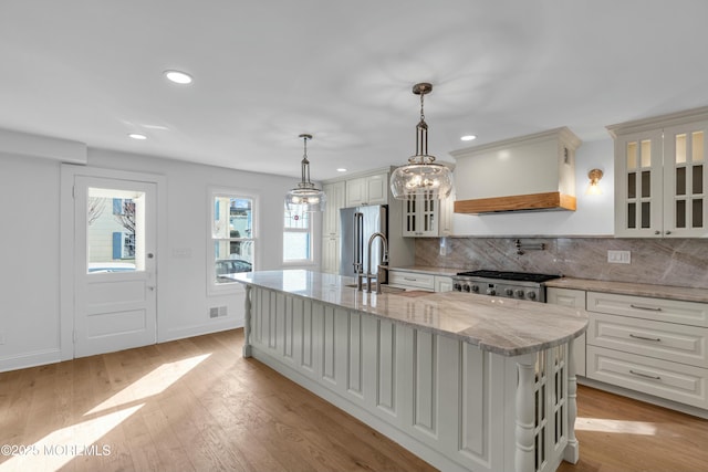 kitchen with stainless steel refrigerator, white cabinetry, an island with sink, sink, and light stone countertops