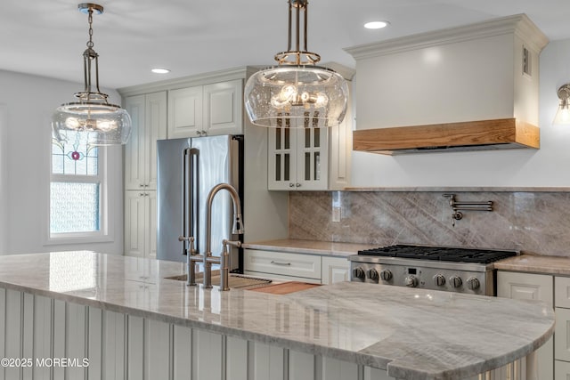 kitchen with custom exhaust hood, light stone counters, high end refrigerator, range, and pendant lighting