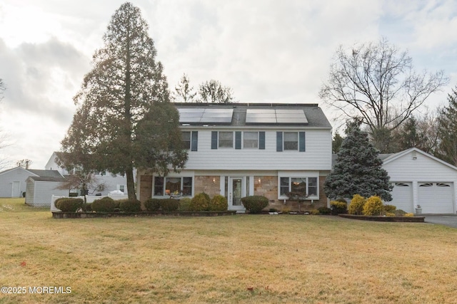 colonial inspired home with stone siding, roof mounted solar panels, a detached garage, and a front lawn