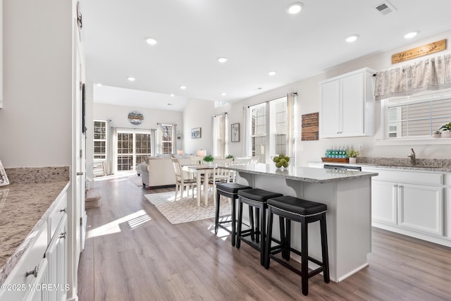 kitchen with plenty of natural light, a center island, light stone countertops, white cabinets, and a kitchen bar