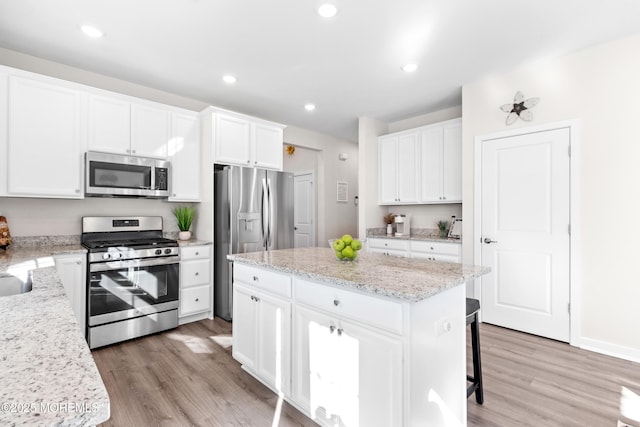 kitchen with a kitchen island, appliances with stainless steel finishes, white cabinets, hardwood / wood-style flooring, and light stone counters