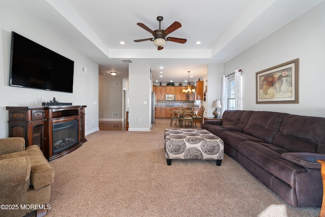 living room featuring a raised ceiling, ceiling fan with notable chandelier, and light carpet