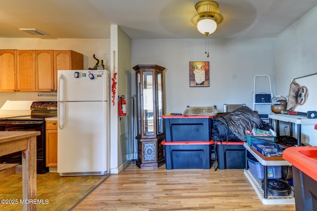 kitchen featuring white refrigerator, black electric range oven, and light hardwood / wood-style floors