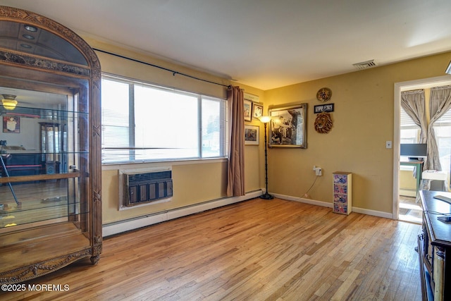 living room with an AC wall unit, baseboard heating, and light hardwood / wood-style flooring