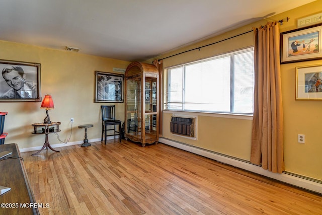 living area with a baseboard heating unit, a wall mounted air conditioner, and light hardwood / wood-style floors