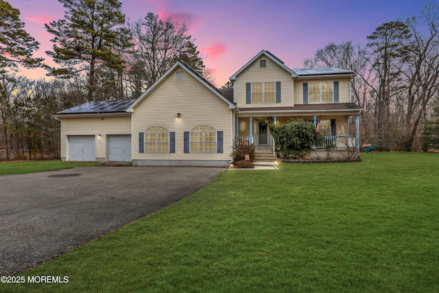 view of front of property with a yard, roof mounted solar panels, a porch, and driveway