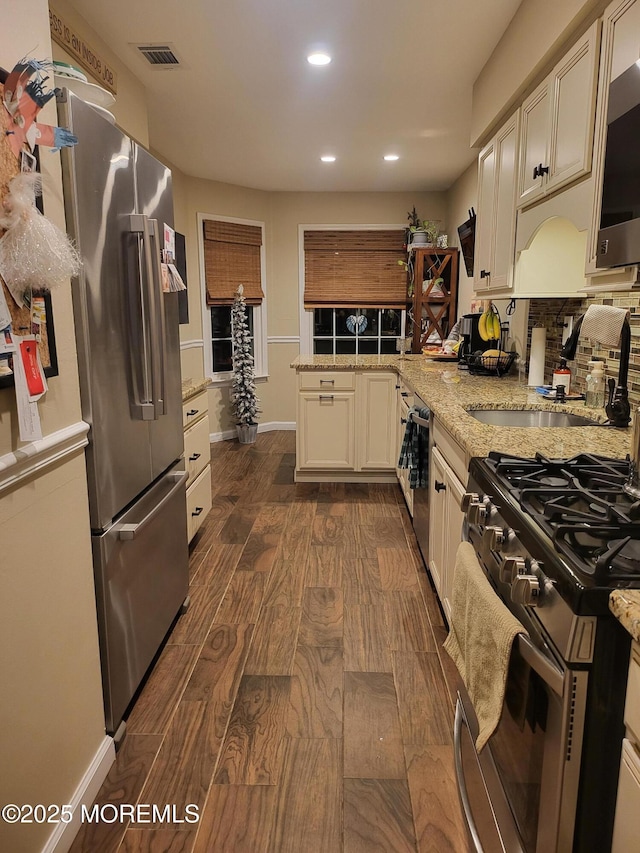 kitchen featuring sink, decorative backsplash, stainless steel appliances, light stone countertops, and dark wood-type flooring