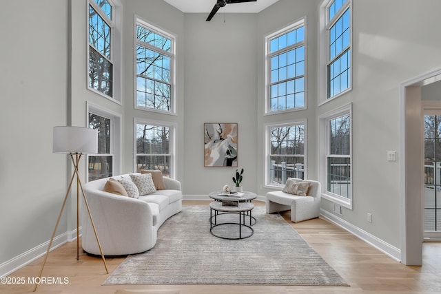 living area with a healthy amount of sunlight, light hardwood / wood-style floors, and a towering ceiling