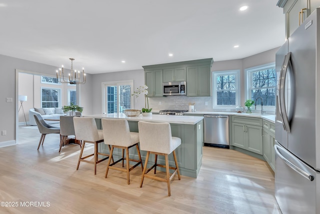 kitchen featuring decorative light fixtures, tasteful backsplash, a center island, stainless steel appliances, and light wood-type flooring