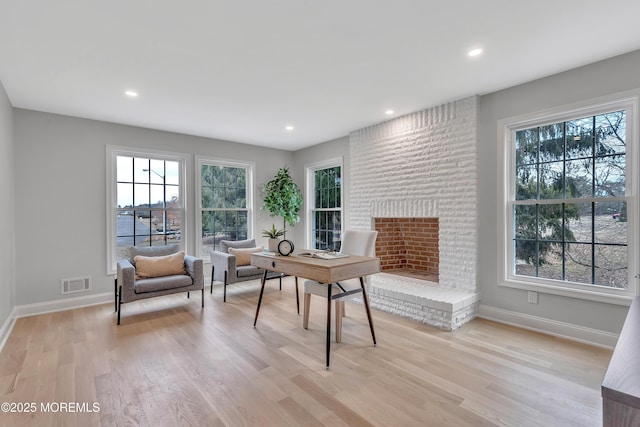 office space with plenty of natural light, a brick fireplace, and light hardwood / wood-style flooring