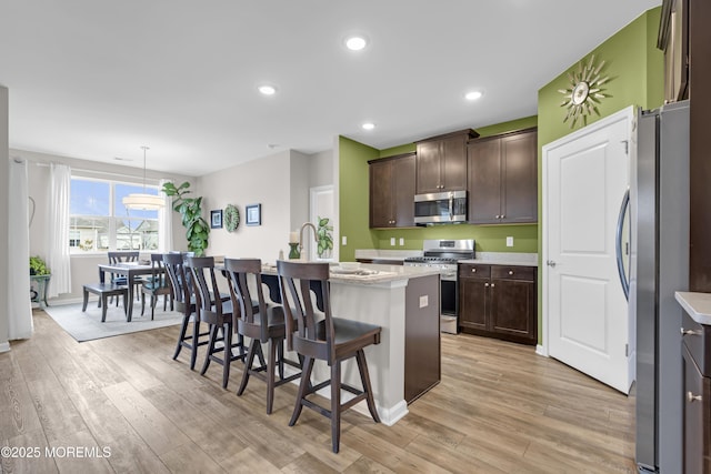 kitchen with appliances with stainless steel finishes, a center island with sink, dark brown cabinetry, and decorative light fixtures