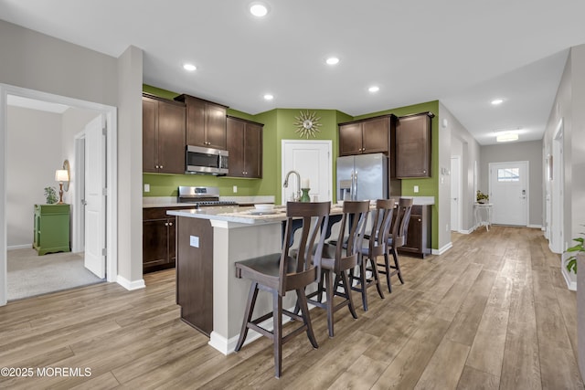 kitchen with light hardwood / wood-style flooring, a breakfast bar, stainless steel appliances, dark brown cabinetry, and a center island with sink