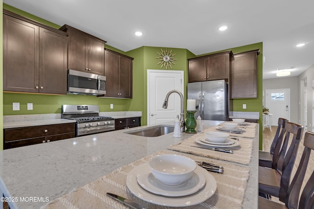 kitchen featuring dark brown cabinetry, sink, appliances with stainless steel finishes, a kitchen breakfast bar, and light stone countertops