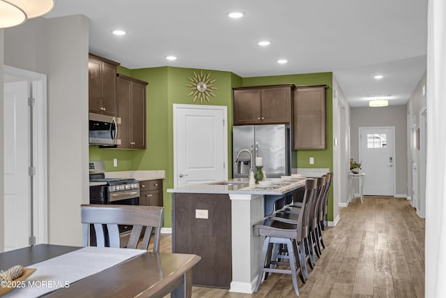 kitchen featuring dark brown cabinetry, a breakfast bar area, a center island with sink, appliances with stainless steel finishes, and light hardwood / wood-style floors