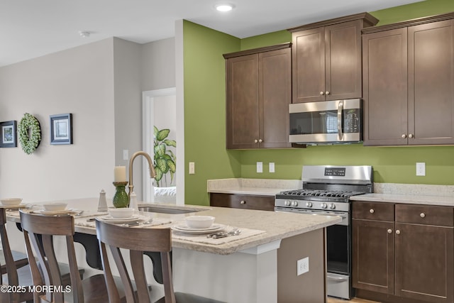 kitchen featuring sink, dark brown cabinets, stainless steel appliances, and a center island with sink